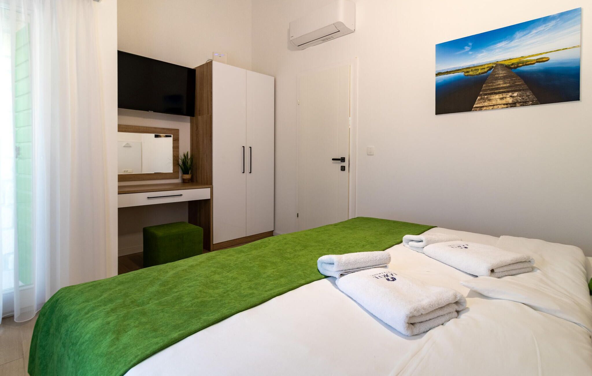 A hotel room with a bed, a desk, a chair, a wardrobe, and a painting on the wall.