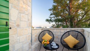 Un balcon avec deux fauteuils en osier, une petite table sur laquelle se trouve un panier de fruits et des tasses, et un mur en pierre.