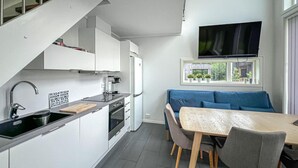 Een compacte keuken met moderne apparatuur, een zithoek met een tafel en stoelen, en een televisie boven een raam.