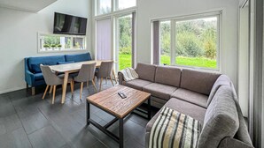 Een moderne woonkamer met een bank, een salontafel, een eettafel met stoelen en een aan de muur bevestigde televisie.