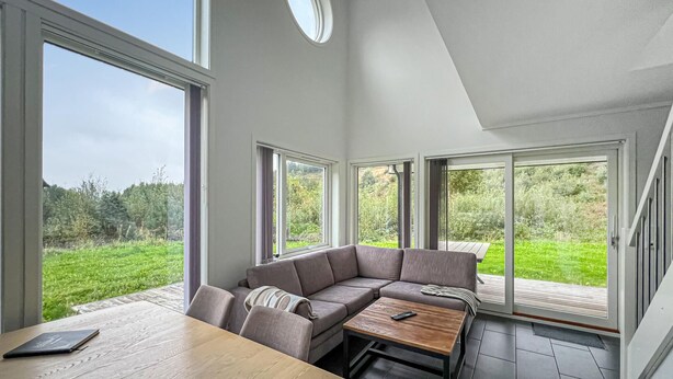 Een moderne woonkamer met een hoekbank, een houten salontafel en grote ramen met uitzicht op een groen landschap.