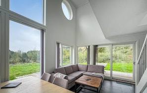 A modern living room with a sectional sofa, a wooden coffee table, and large windows offering a view of a green landscape. - Gorgeous home in Svenevig with WiFi (Svenevig)