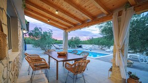 Ein überdachter Außenbereich mit Pool, Korbstühlen und einem Tisch.