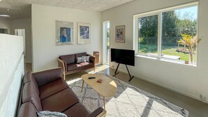 Una sala de estar con un sofá de cuero marrón, una mesa de centro de madera y un televisor de pantalla plana. Hay cuadros enmarcados en la pared y un ventanal con vistas al exterior.