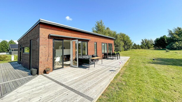 Una casa moderna con terraza de madera, grandes puertas correderas de vidrio y mobiliario exterior.
