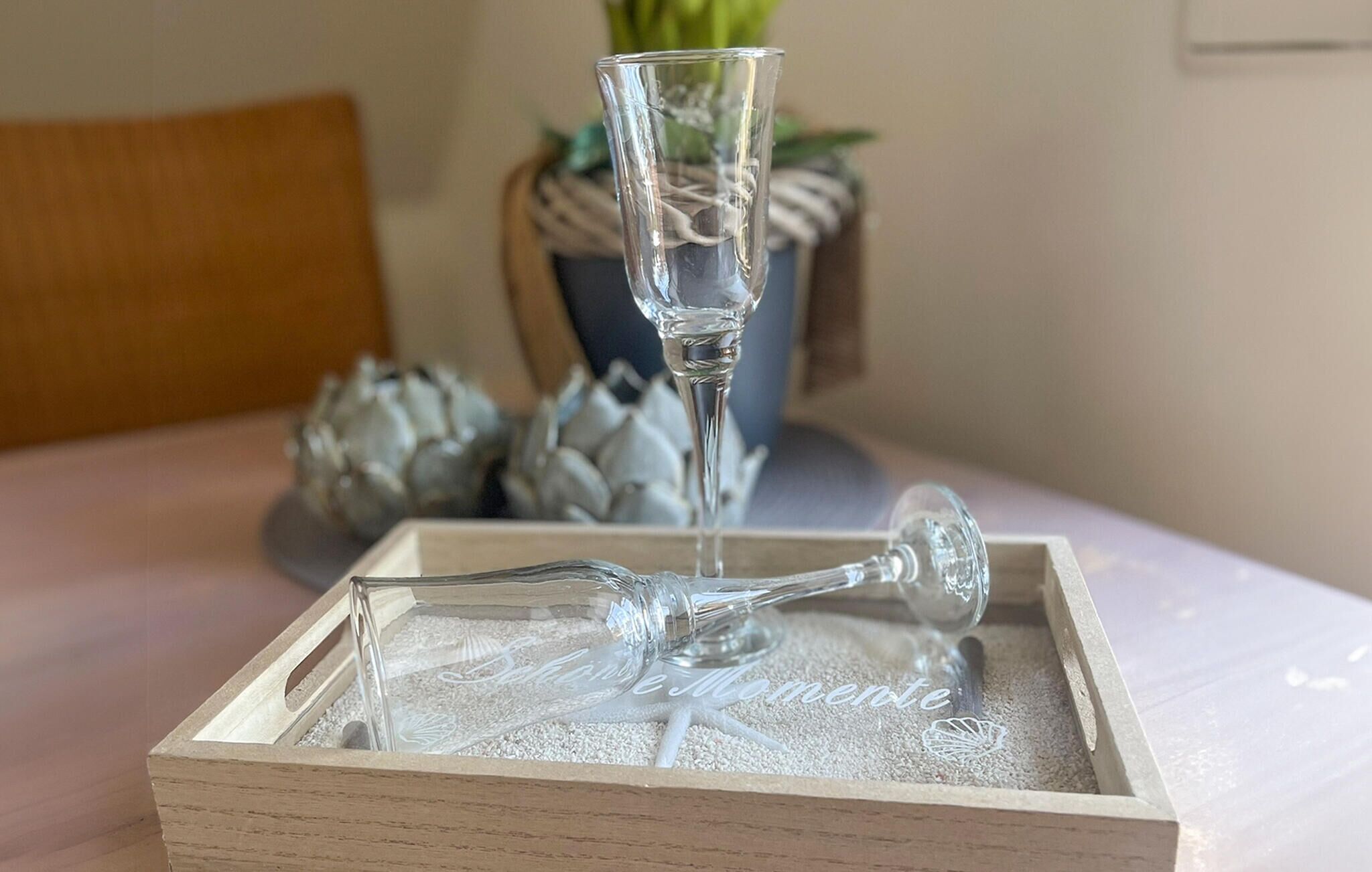 En klar glasflaske på en træbakke med sand, et glas og dekorative skaller i baggrunden.