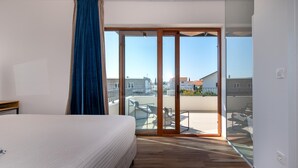 Ett hotellrum med en säng, en stor skjutdörr i glas som leder ut till en balkong och utsikt över de omgivande byggnaderna.