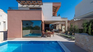 Ett modernt hus med en swimmingpool, utomhusmöbler och en stenmur.