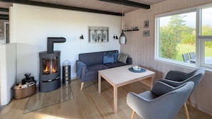 A cozy living room with a wood-burning stove, a sofa, a table, and chairs. - 3 bedroom awesome home in Tarm (Tarm)