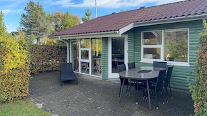 A wooden house with a tiled roof, a glass door leading to an outdoor seating area with a table and chairs. - 3 bedroom awesome home in Tarm (Tarm)