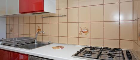 A kitchen with a gas stove, a sink, and red cabinets.