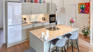 Una cocina moderna con una isla central, taburetes de bar, horno empotrado y un lavamanos.