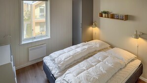 Un dormitorio con cama, ventana, radiador, escritorio y estanterías con objetos.