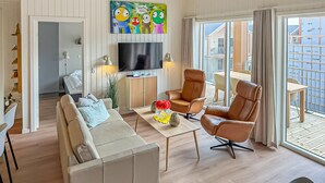 Una sala de estar moderna con sofá, sillones, televisor, comedor y balcón con vistas.