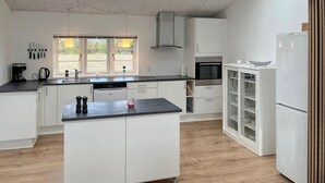 Una cuina moderna amb armaris blancs, una illa central i forn integrat.