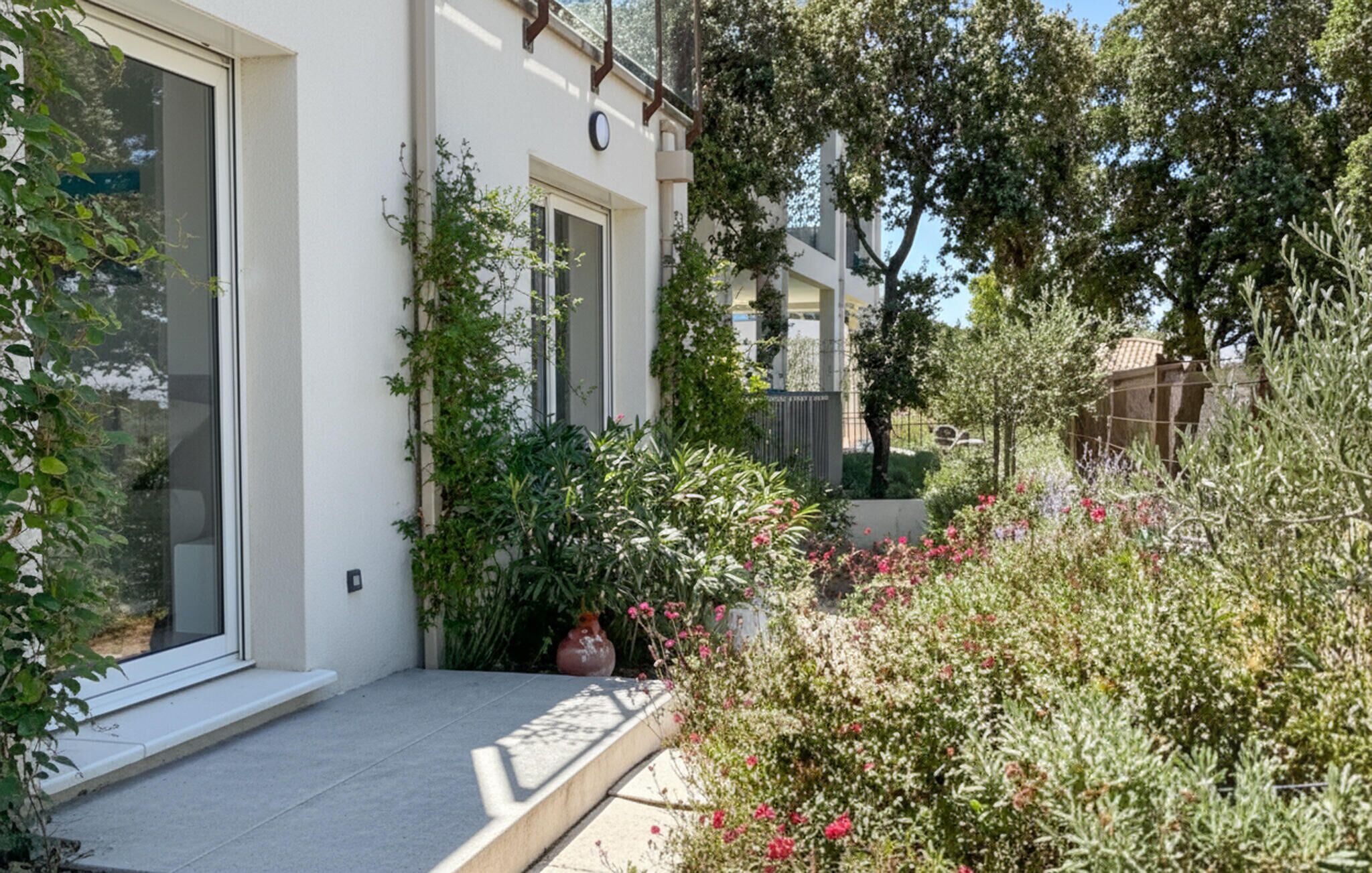 A residential building with a white exterior, large windows, and a small garden area with various plants and flowers.