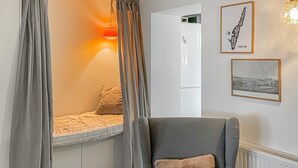 Quarto com uma cama, uma poltrona cinza e uma janela com cortinas.
