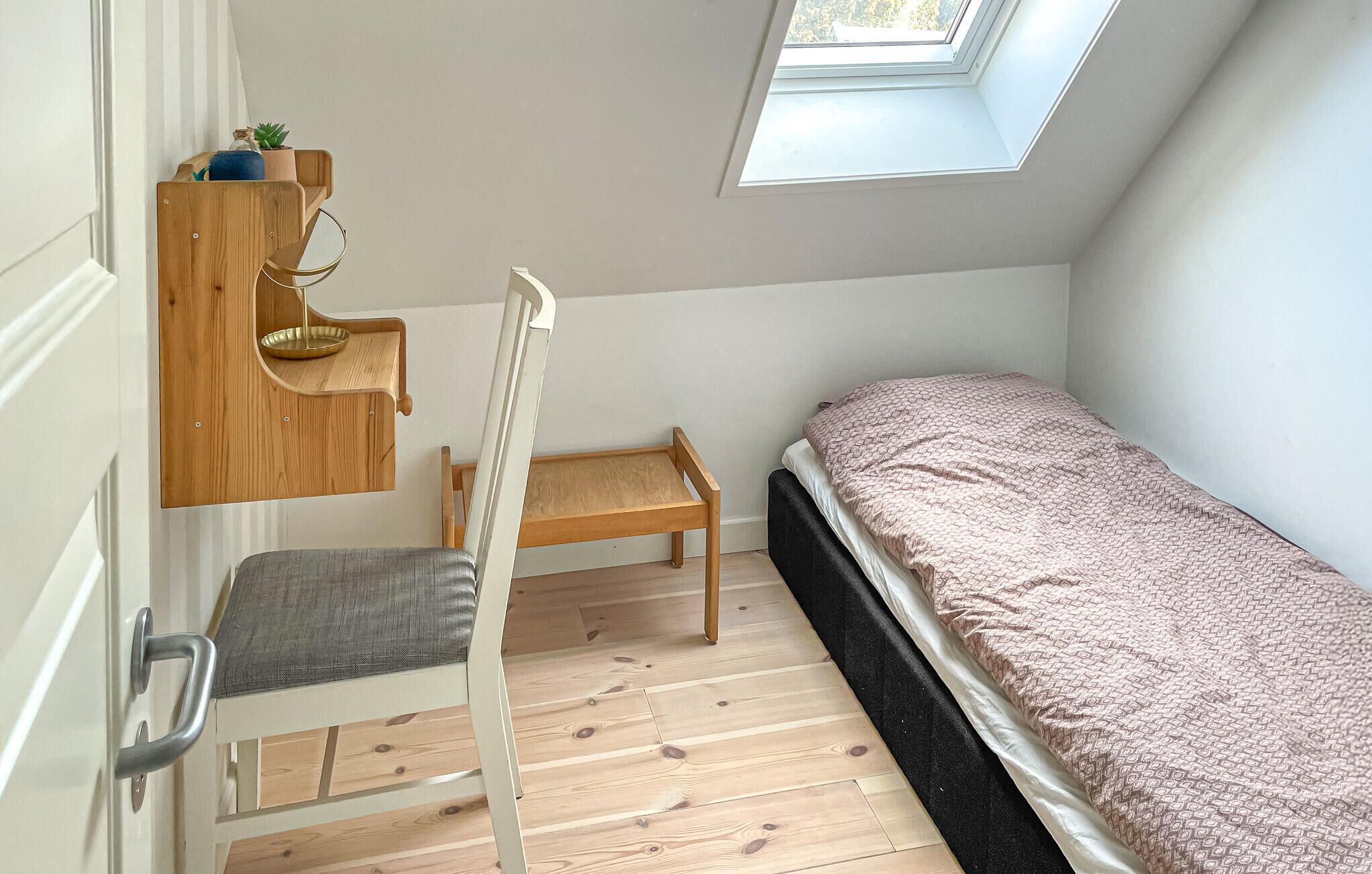 Une petite pièce bien rangée, avec un lit superposé, un bureau en bois avec une chaise et une lucarne.