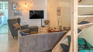 Uma sala de estar moderna com um sofá cinzento, uma televisão e um espaço de refeições com mesa e cadeiras.