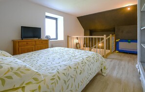 Ein Schlafzimmer mit Bett, Kommode, Fernseher, Fenster und einer Treppe zu einer oberen Ebene.