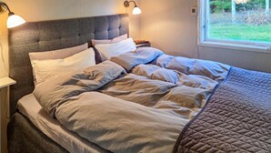 A neatly made bed with a grey headboard, two bedside lamps, and a window with a view of greenery. - 1 bedroom awesome home in Boxholm (Boxholm)