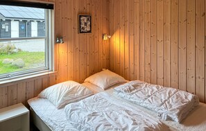 Une chambre avec des murs en bois, un lit avec une literie blanche, une fenêtre et une petite table de chevet.