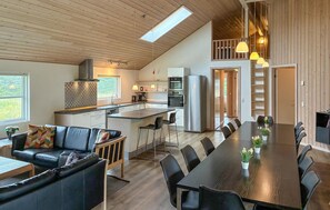Une cuisine moderne dotée d’un îlot central, un coin repas avec une longue table et des chaises, et un espace en mezzanine accessible par un escalier.