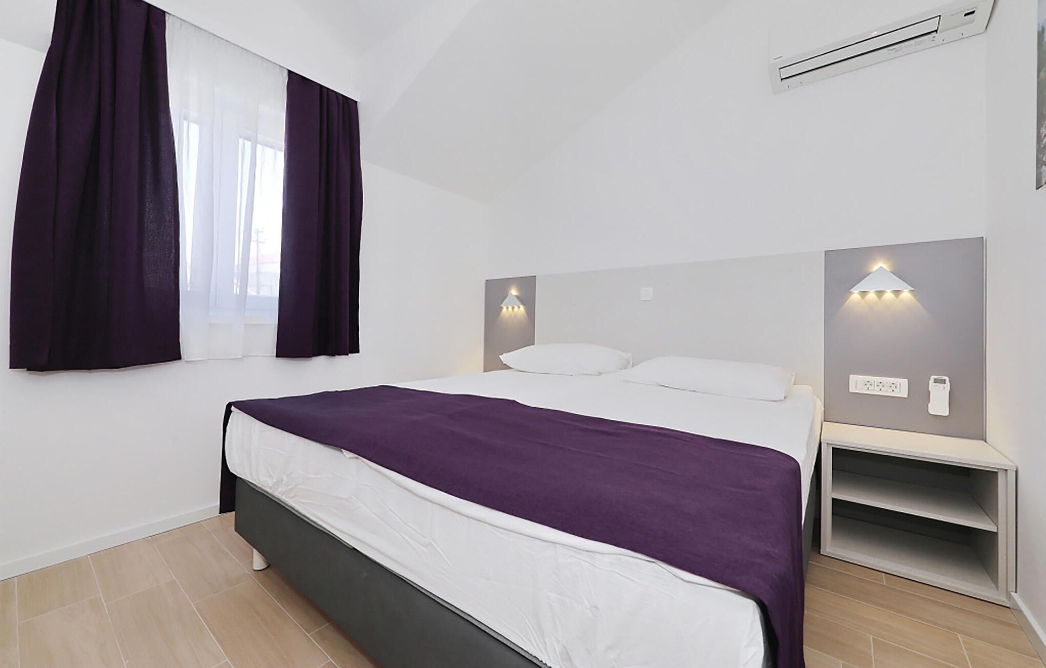 Ein modernes Schlafzimmer mit einem Bett, zwei Nachttischen, einem Fenster mit Vorhängen und einer Wandleuchte.