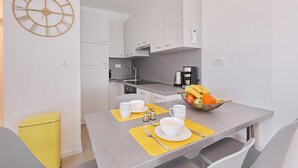 Una cucina compatta con mobili bianchi, una macchina da caffè e una ciotola di frutta sul piano di lavoro.