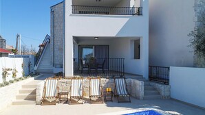 Una moderna casa a due piani con piscina, gradini in pietra e area salotto all'aperto.