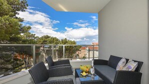 A balcony with wicker furniture, a glass table, and a view of trees and buildings. - Nice apartment in Makarska with WiFi (Makarska)