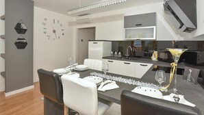 A modern kitchen with a microwave, stove, and sink. There is a dining area with a table set for two, and a clock on the wall. - Nice apartment in Makarska with WiFi (Makarska)