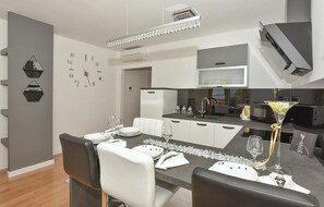 A modern kitchen with a microwave, stove, and sink. There is a dining area with a table set for two, and a clock on the wall. - Nice apartment in Makarska with WiFi (Makarska)