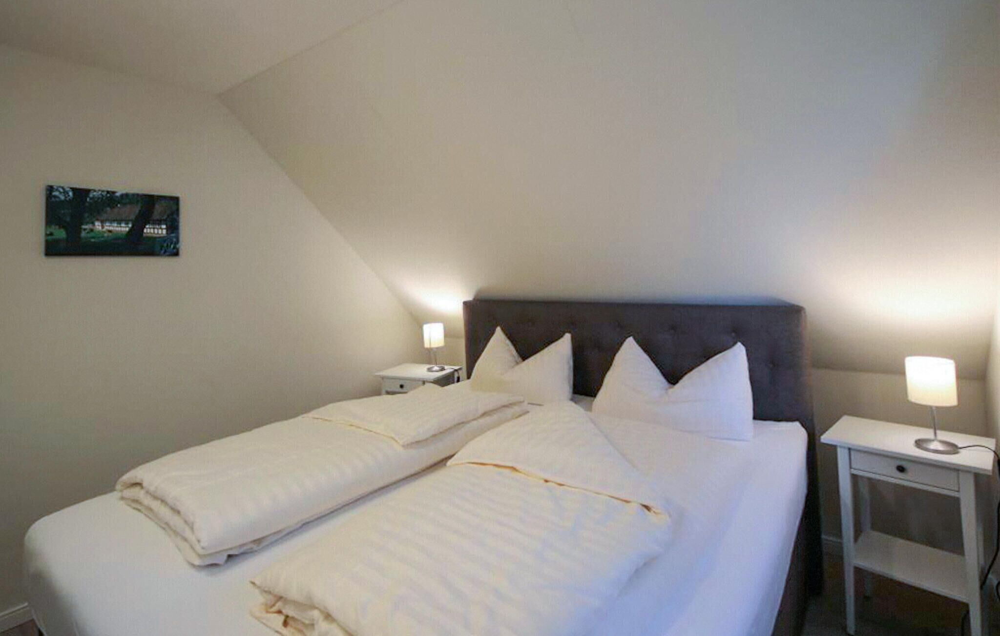 A neatly made bed with white linens and pillows, two bedside tables with lamps, and a framed picture on the wall.