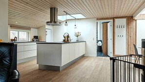 Una cocina moderna con una isla central, techo de madera y vista al comedor.