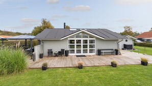 Una casa moderna con una amplia terraza, un patio cubierto y un césped bien cuidado.