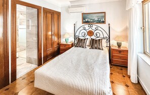 Une chambre à coucher comprenant un lit, deux tables de chevet, une armoire en bois, une fenêtre avec des rideaux et un climatiseur fixé au mur.