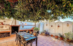 Une terrasse extérieure avec un barbecue en briques, une table à manger pour quatre personnes et des plantes en pot.