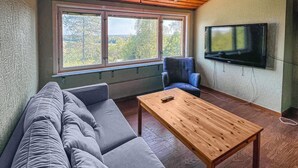 Een kamer met een bank, een houten tafel, een blauwe stoel en een aan de muur bevestigde televisie.
