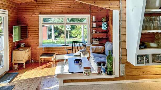 A cozy cabin interior with a wooden interior, a dining area with a table and chairs, a sofa, a small kitchen area with a coffee maker, and a window with a view of the outdoors. - Lovely home in Asnæs with WiFi (Asnæs)