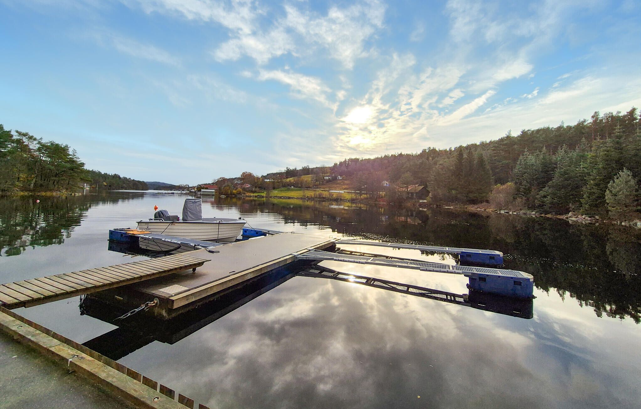 Un lac paisible, avec un quai et des bateaux, entouré de collines boisées et surplombé d’un ciel dégagé.