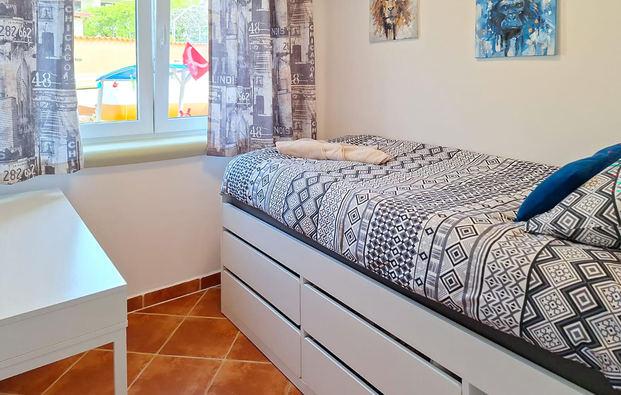 Een slaapkamer met een bed, een wit bureau en een raam met gordijnen.