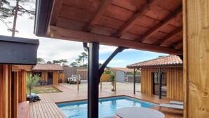Eine Holzterrasse mit Pool, Sitzgelegenheiten im Freien und einem überdachten Bereich mit Tisch und Stühlen.