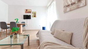 Un salon moderne avec un canapé, une table basse en verre et un coin repas comprenant des chaises et un téléviseur.