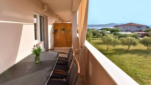 Un balcon avec une table et des chaises, une cloison en bois et une vue sur la mer et la verdure.