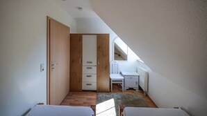 A small, well-lit attic bedroom with a sloped ceiling, a wooden wardrobe, a white desk, and a radiator.