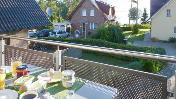 A balcony with breakfast items, a view of houses, and parked cars.