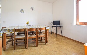 Ein Essbereich mit einem runden Tisch, Holzsesseln, einem Ventilator und einem Fernseher auf einem Schrank.