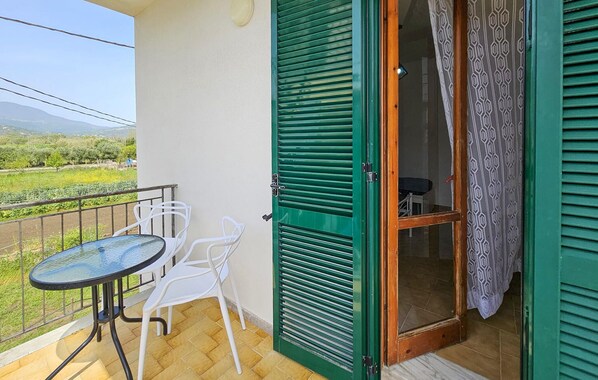 Ein Balkon mit Tisch und Stühlen, eine grüne Tür und Blick ins Grüne.