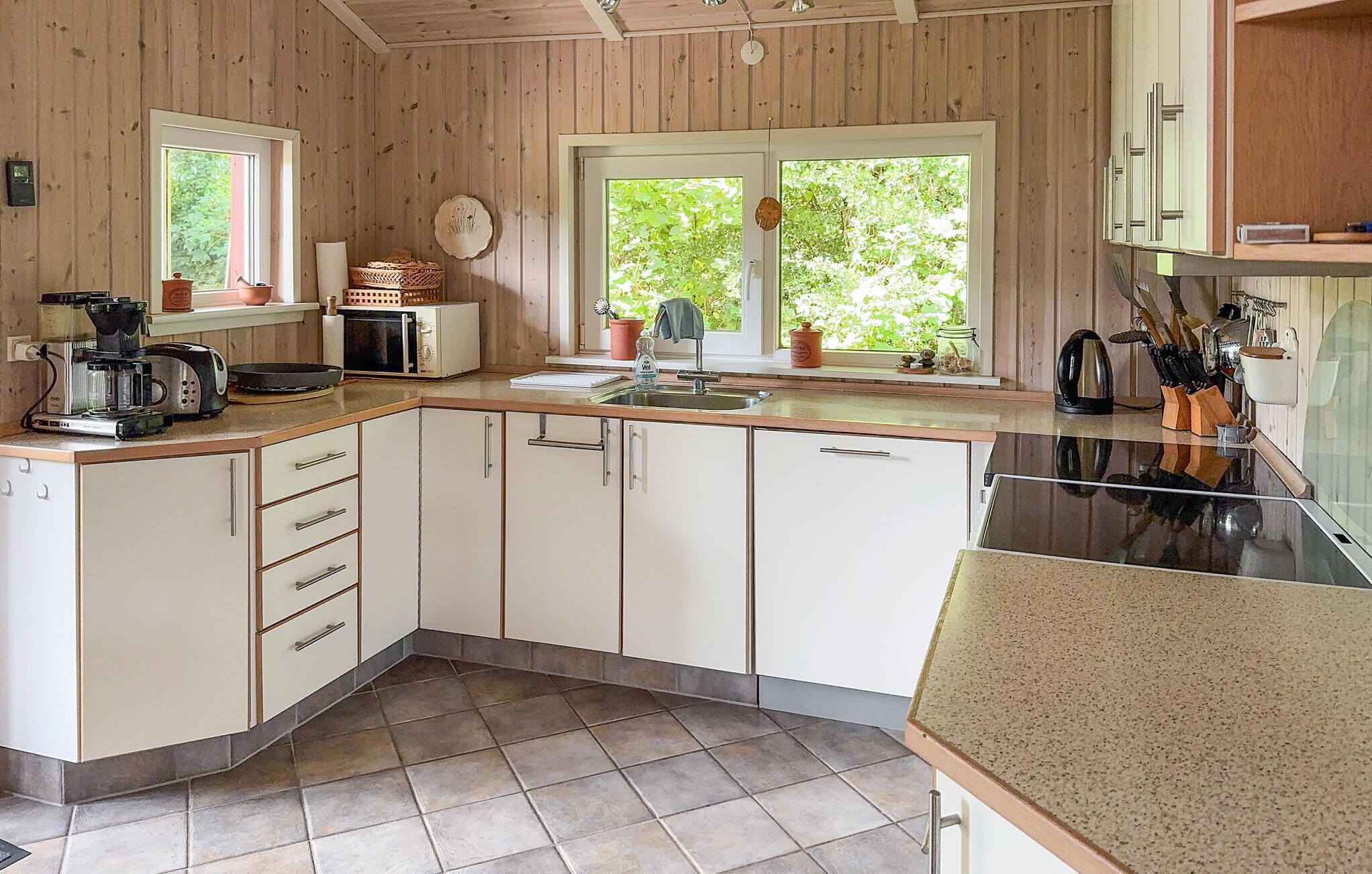 Een keuken met houten wanden, een spoelbak, kastjes, een fornuis en een raam met uitzicht op groen.